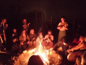 Un gruppo di volontari e volontarie fanno musica davanti un fuoco
