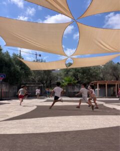 bambini e bambine che giocano a calcio in un luogo aperto con dei tendoni che coprono il cielo 
