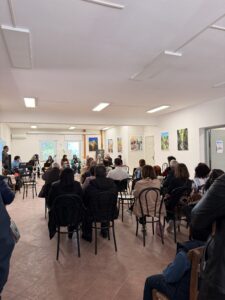 gruppo di persone sedute rivolte verso un altro gruppo di persone con strumenti musicali a loro volta sedute in una sala